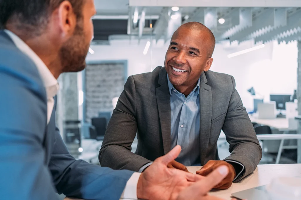A businessman consulting with a male client in an office setting, representing SAI MedPartner's global consulting teams.