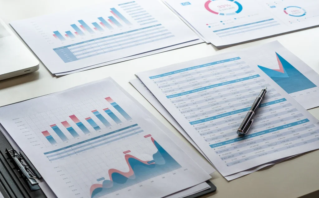 Stacks of printed reports with charts and graphs on a desk, symbolizing PharmaForce International's syndicated benchmarking reports.